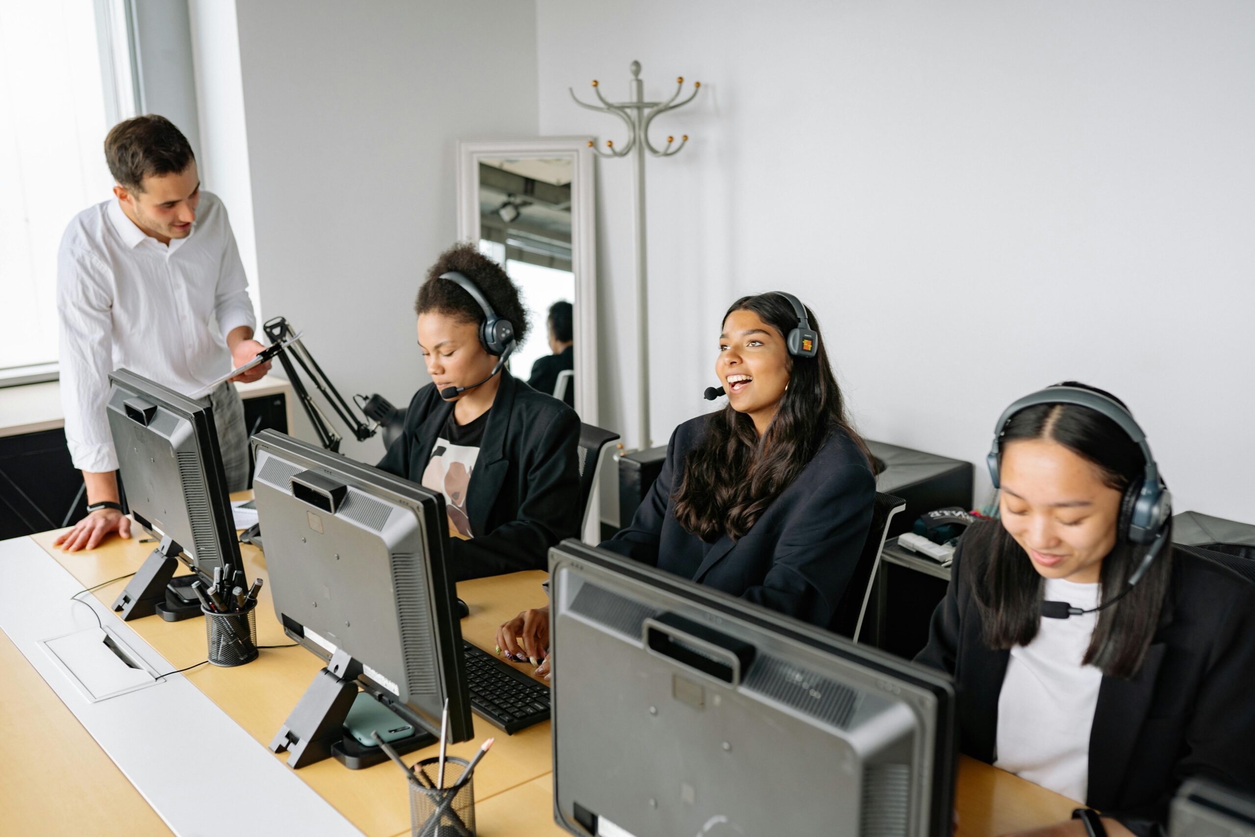 A diverse team of customer service representatives working in an office setting, wearing headsets and using computers.